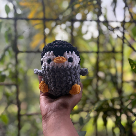 Hand holding a small crochet penguin toy with a blurred natural background
