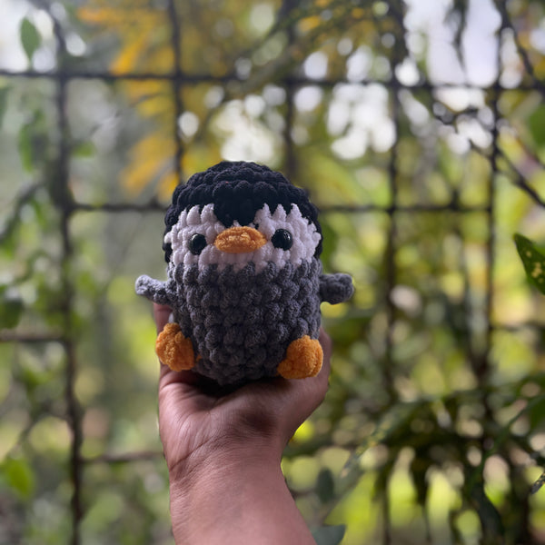 Hand holding a small crochet penguin toy with a blurred natural background
