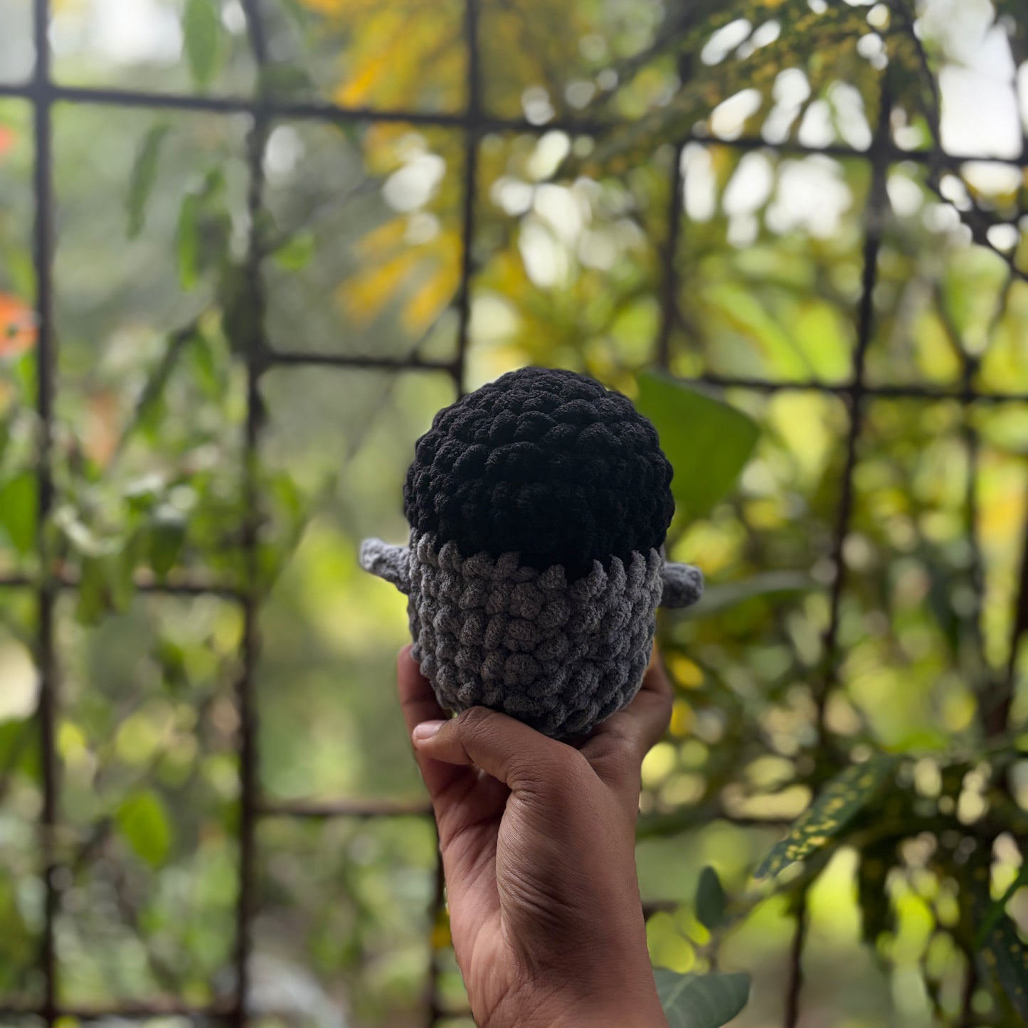 Hand holding back of a small crochet penguin toy with a blurred natural background