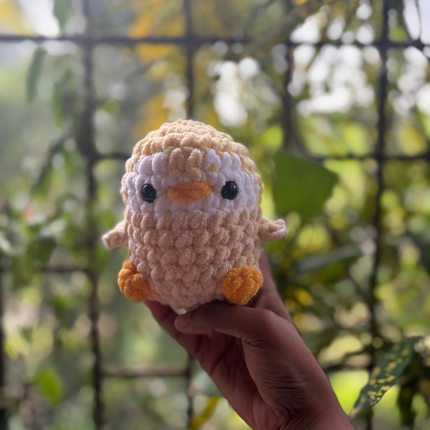 Hand holding a small crochet penguin toy with a blurred natural background