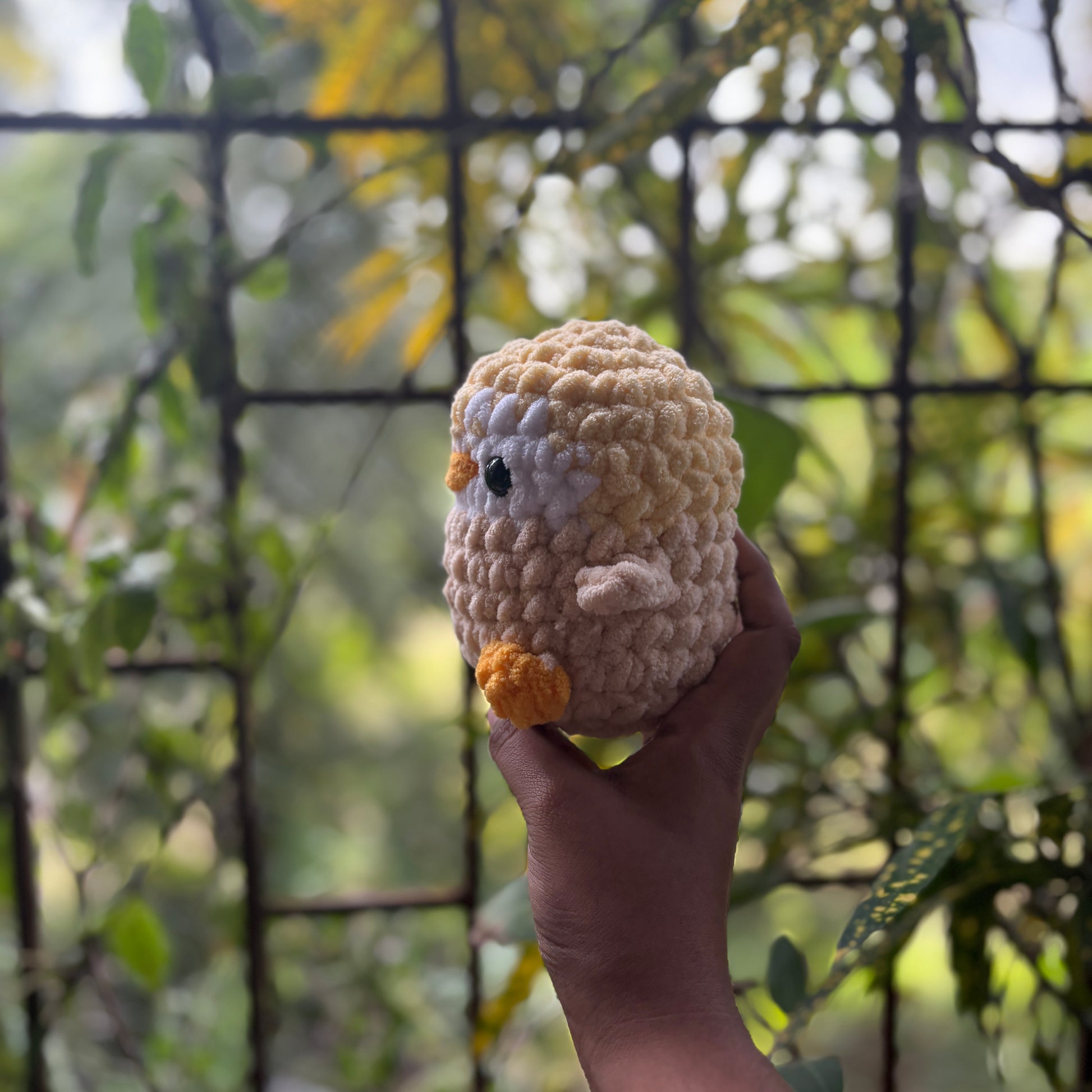 Hand holding a small crochet penguin toy with a blurred natural background