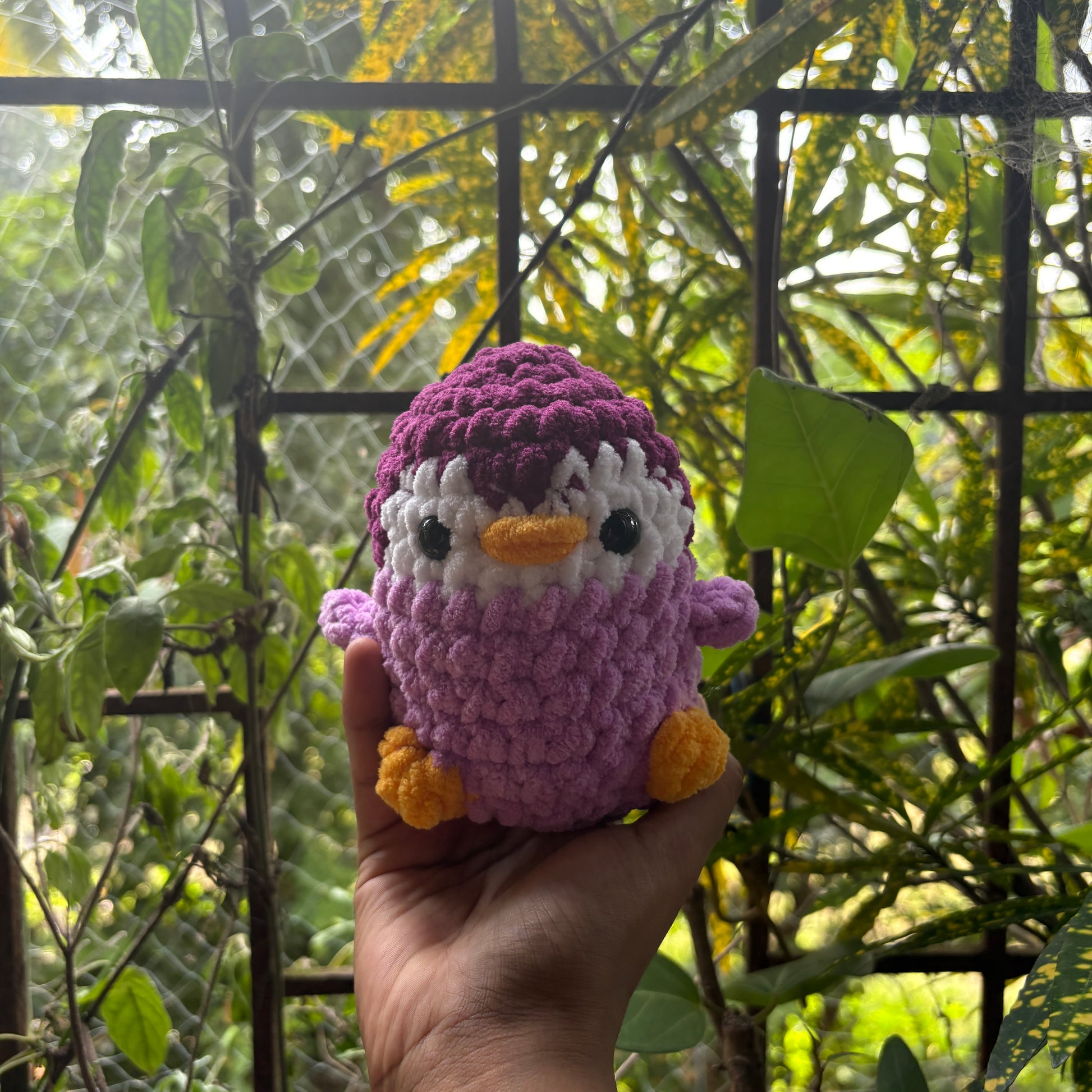 Hand holding a small crochet penguin toy with a blurred natural background