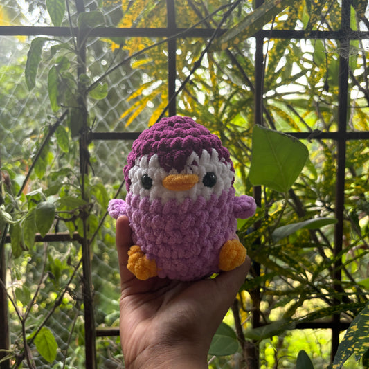 Hand holding a small crochet penguin toy with a blurred natural background