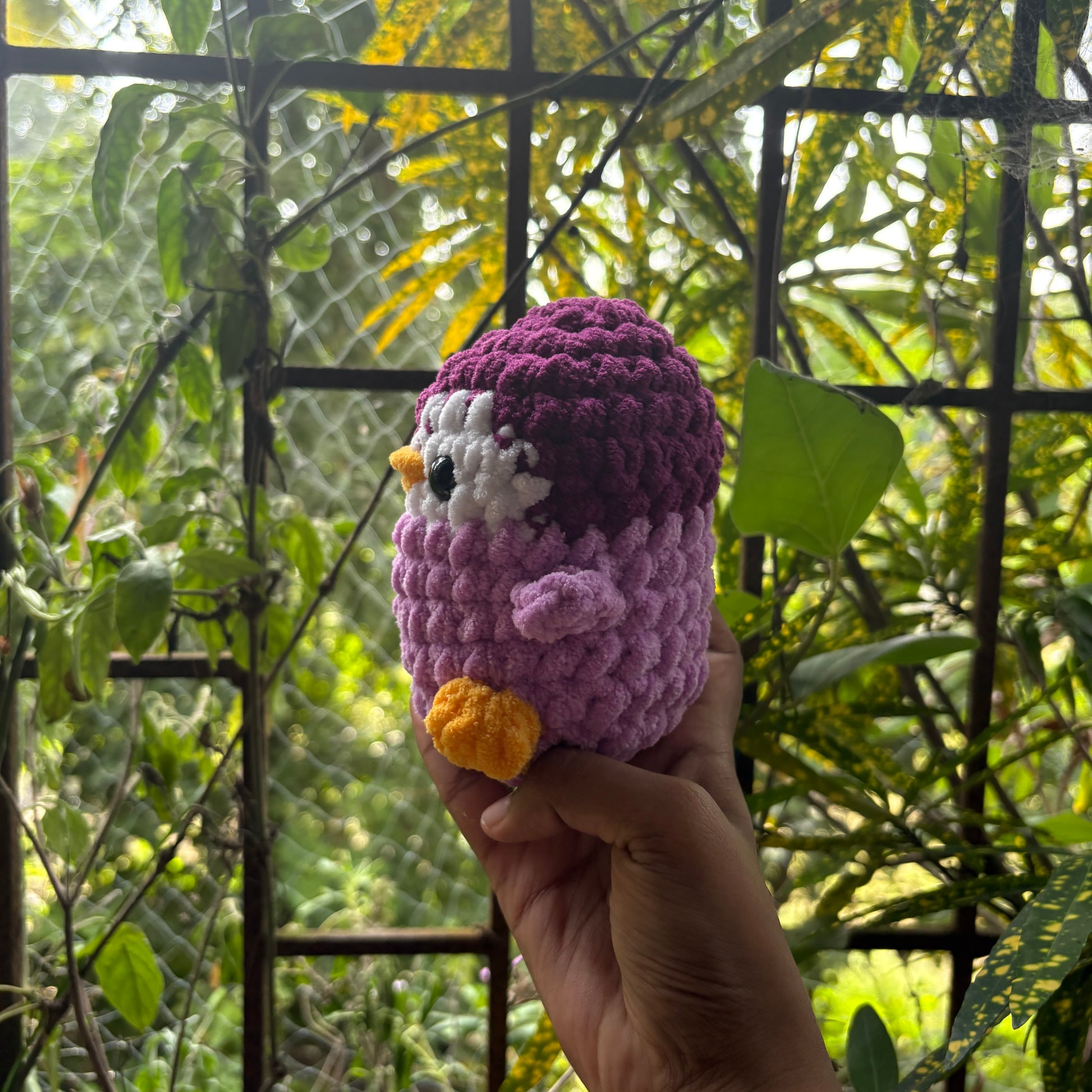 Hand holding a small crochet penguin toy with a blurred natural background