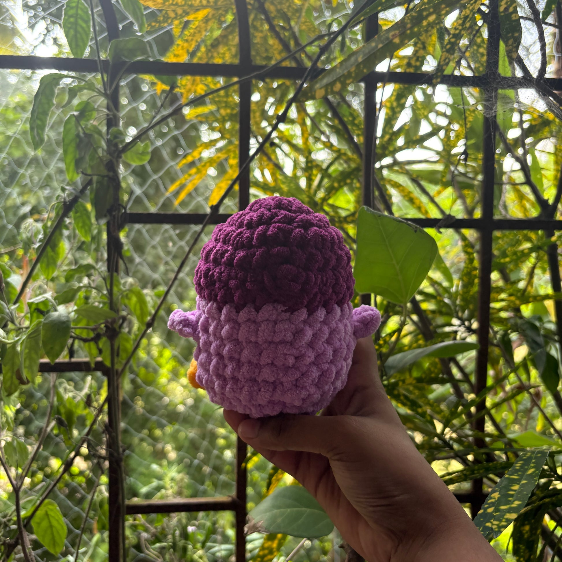 Hand holding a small crochet penguin toy with a blurred natural background
