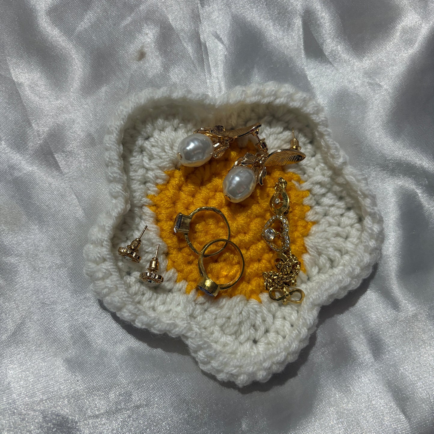 Jewelry displayed on a crocheted flower with white and yellow colors against a textured gray background.