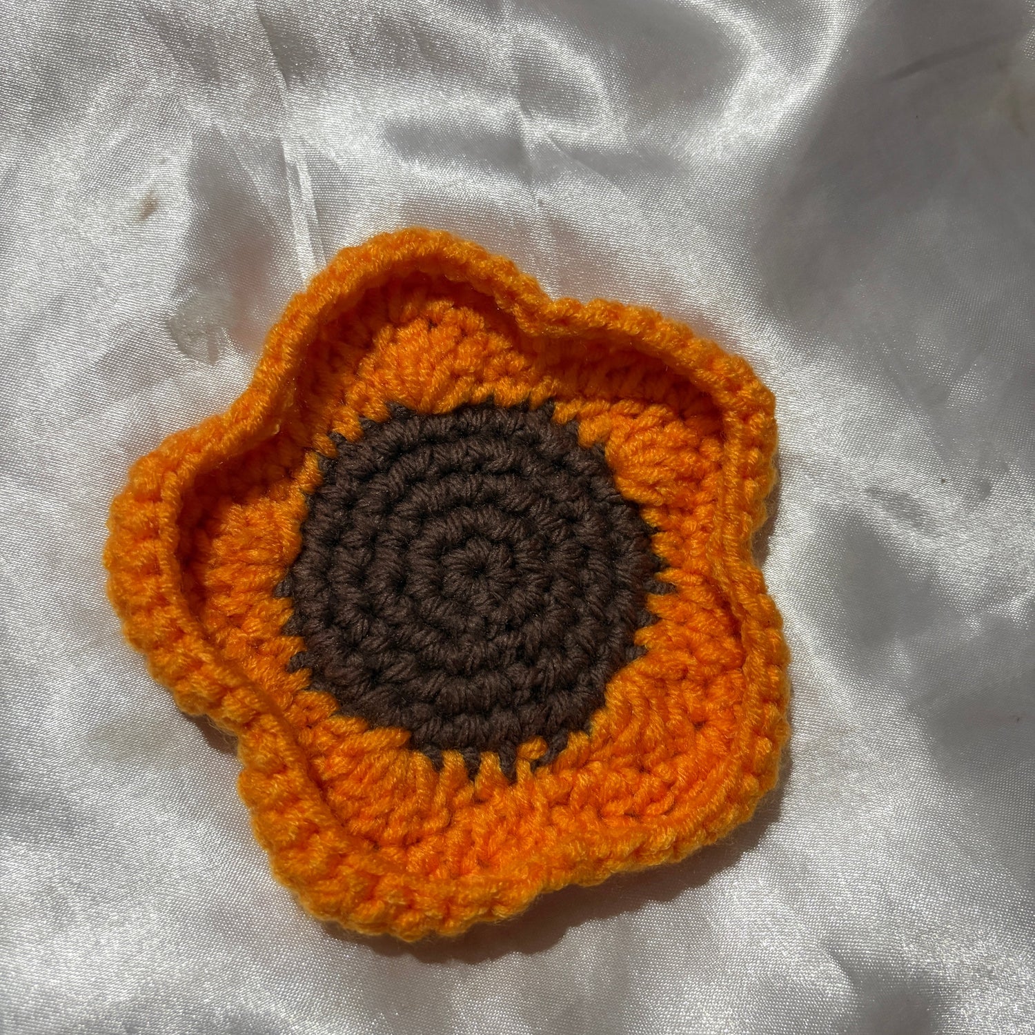Crocheted flower with orange petals and brown center on a white fabric background