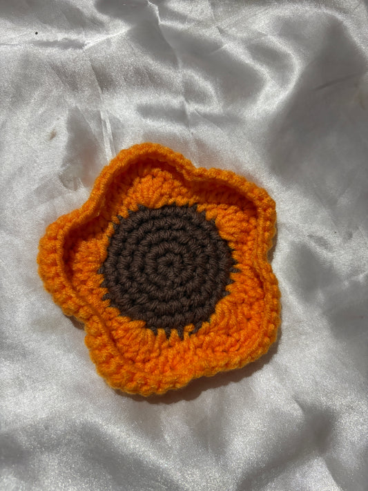Crocheted flower with orange petals and brown center on a white fabric background