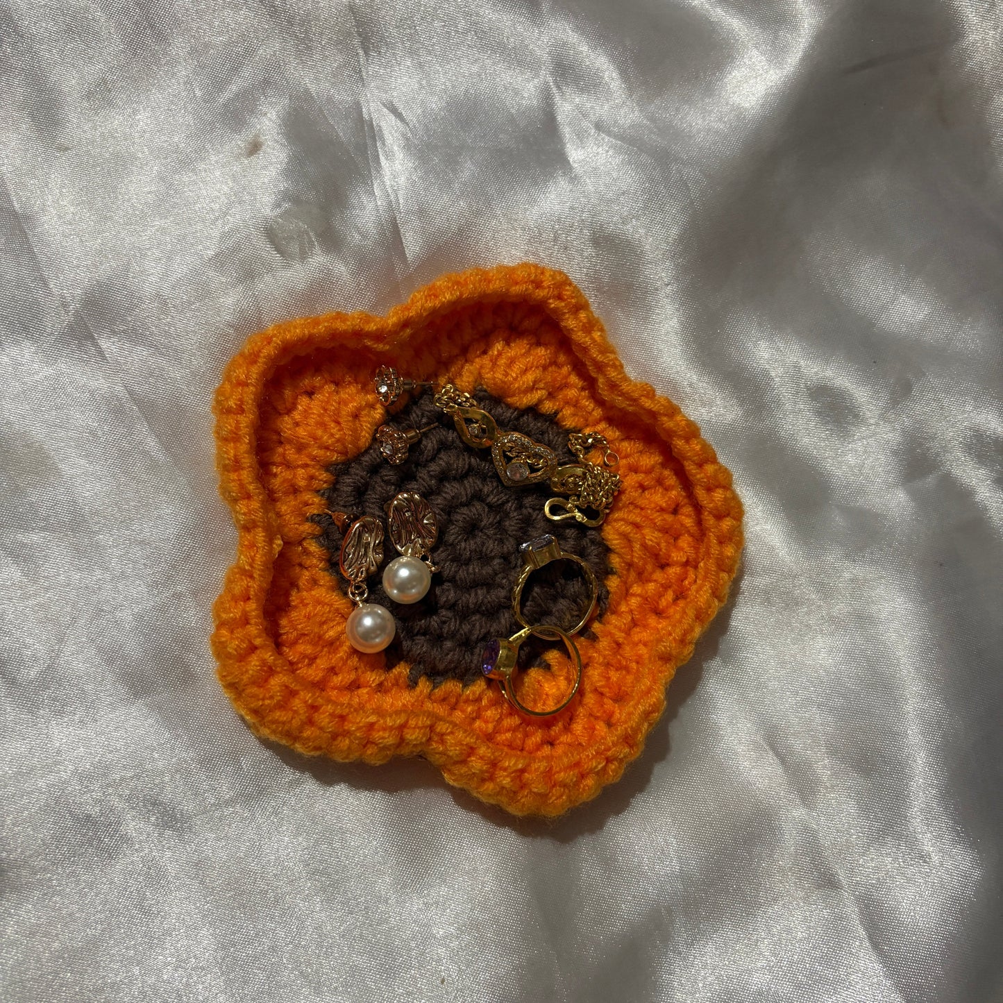 Crocheted orange flower with embedded jewelry on a textured white surface