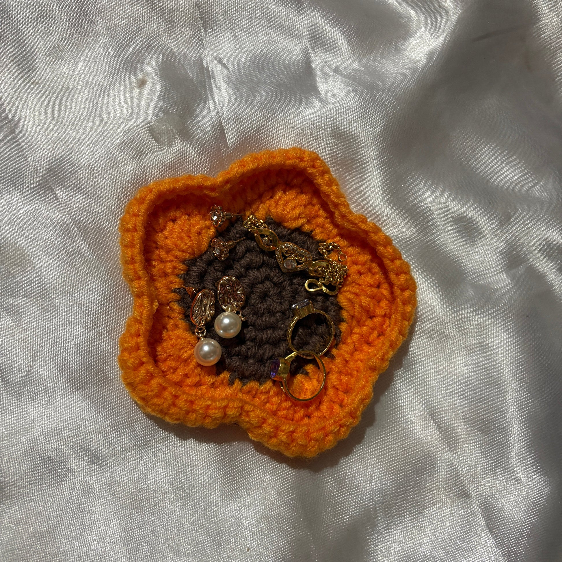 Crocheted orange flower with embedded jewelry on a textured white surface