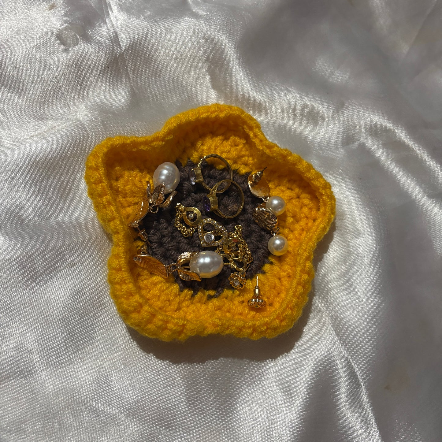 Yellow crocheted flower with jewelry on a white fabric background