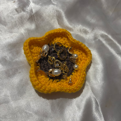 Yellow crocheted flower with jewelry on a white fabric background