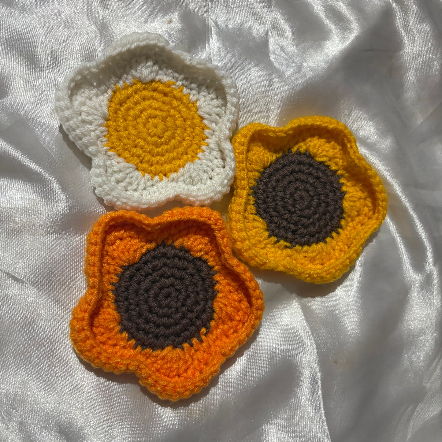 Three crocheted flowers in white, yellow, and orange on a white fabric background