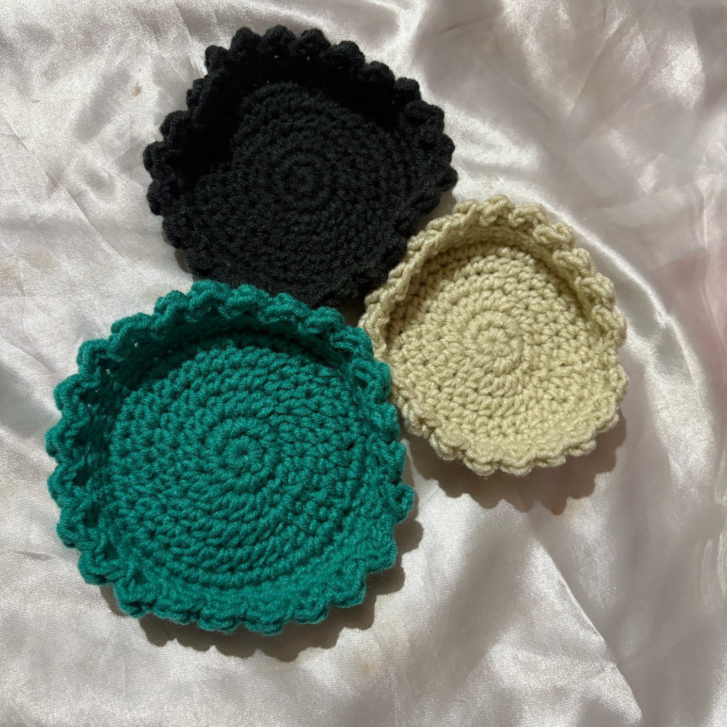 Three crocheted bowl in black, green, and beige on a white fabric background