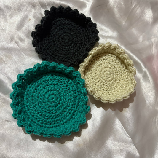 Three crocheted bowl in black, green, and beige on a white fabric background