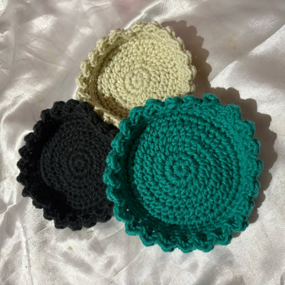 Three crocheted trinket bowl in black, beige, and teal on a white fabric background
