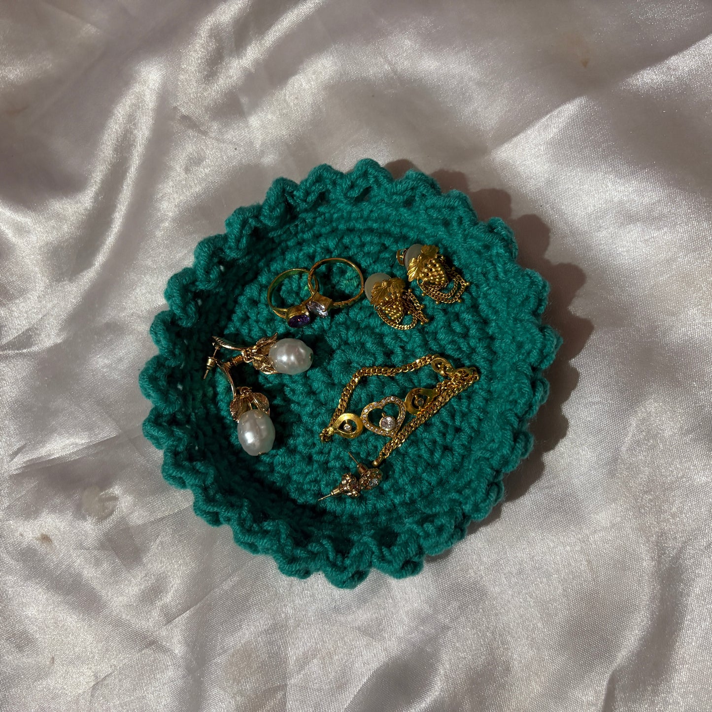 Teal crocheted jewelry holder with gold and pearl jewelry on a white fabric background