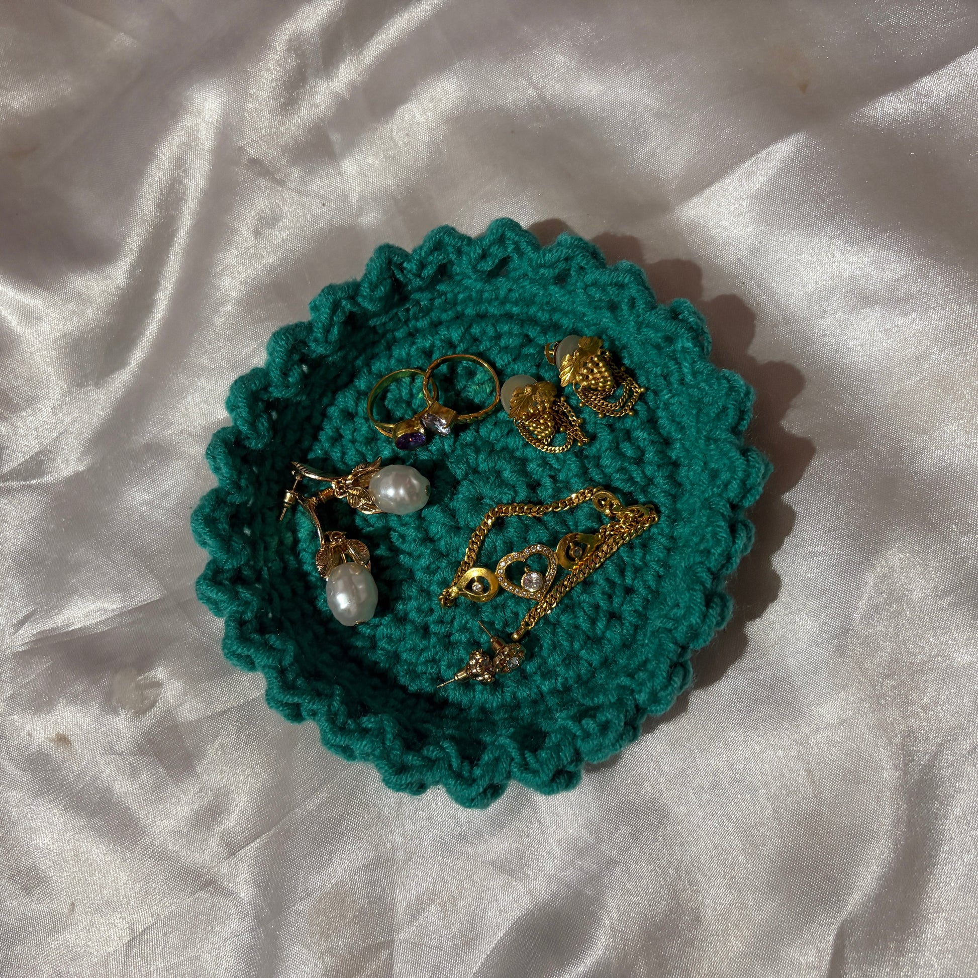 Teal crocheted jewelry holder with gold and pearl jewelry on a white fabric background