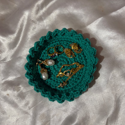 Teal crocheted jewelry holder with gold and pearl jewelry on a white fabric background