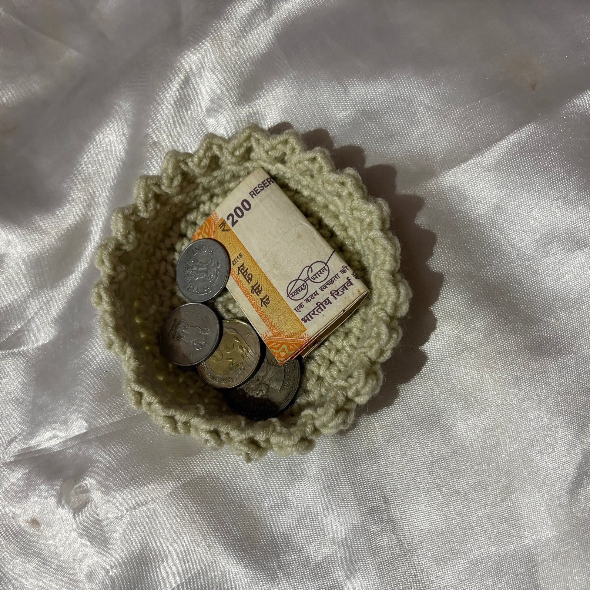 Small crocheted bowl with coins and a banknote on a white fabric background