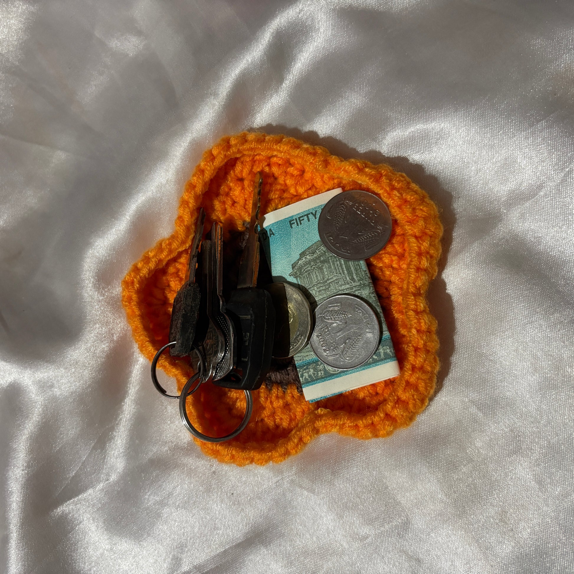 Orange crochet coin purse with keys and money on a white fabric background