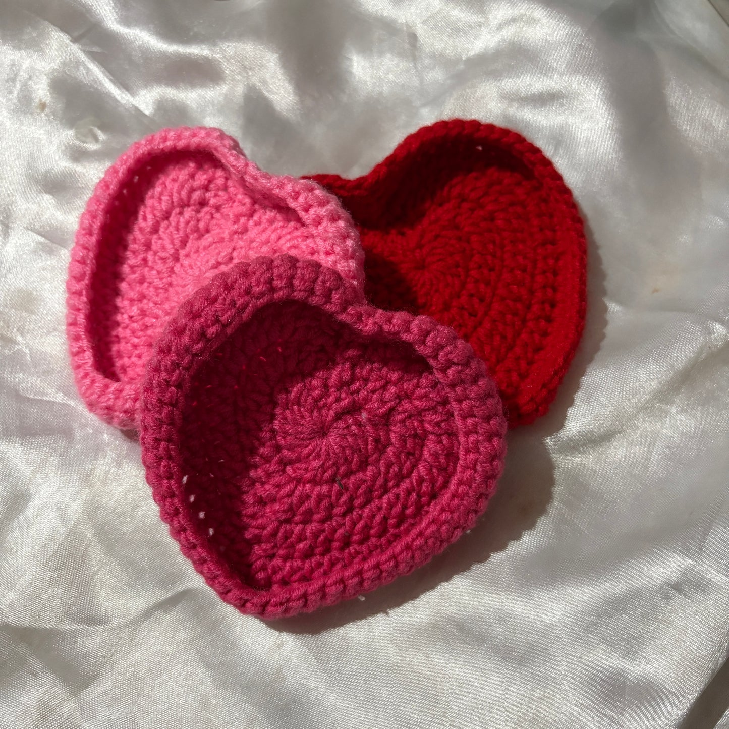 crochet heart-shaped jwellery holder in pink and red on a white fabric background