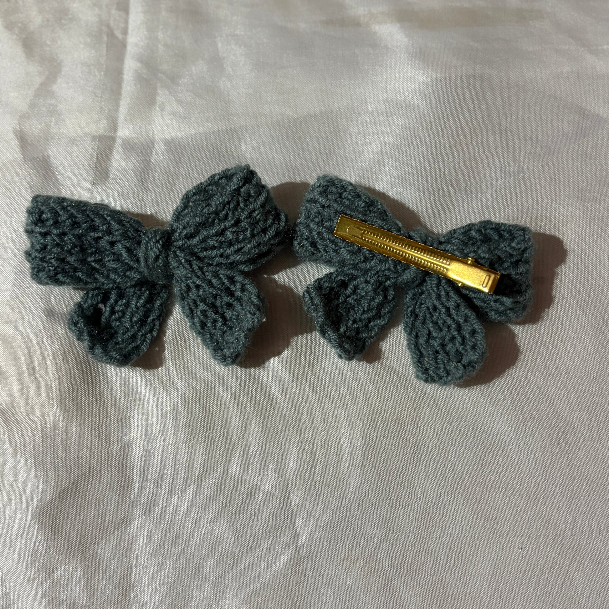 Two crocheted hair bows with gold clips on a light fabric background