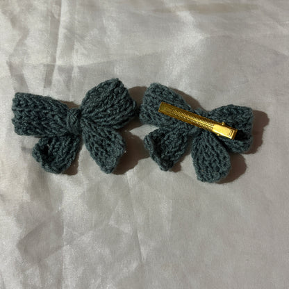 Two crocheted hair bows with gold clips on a light fabric background