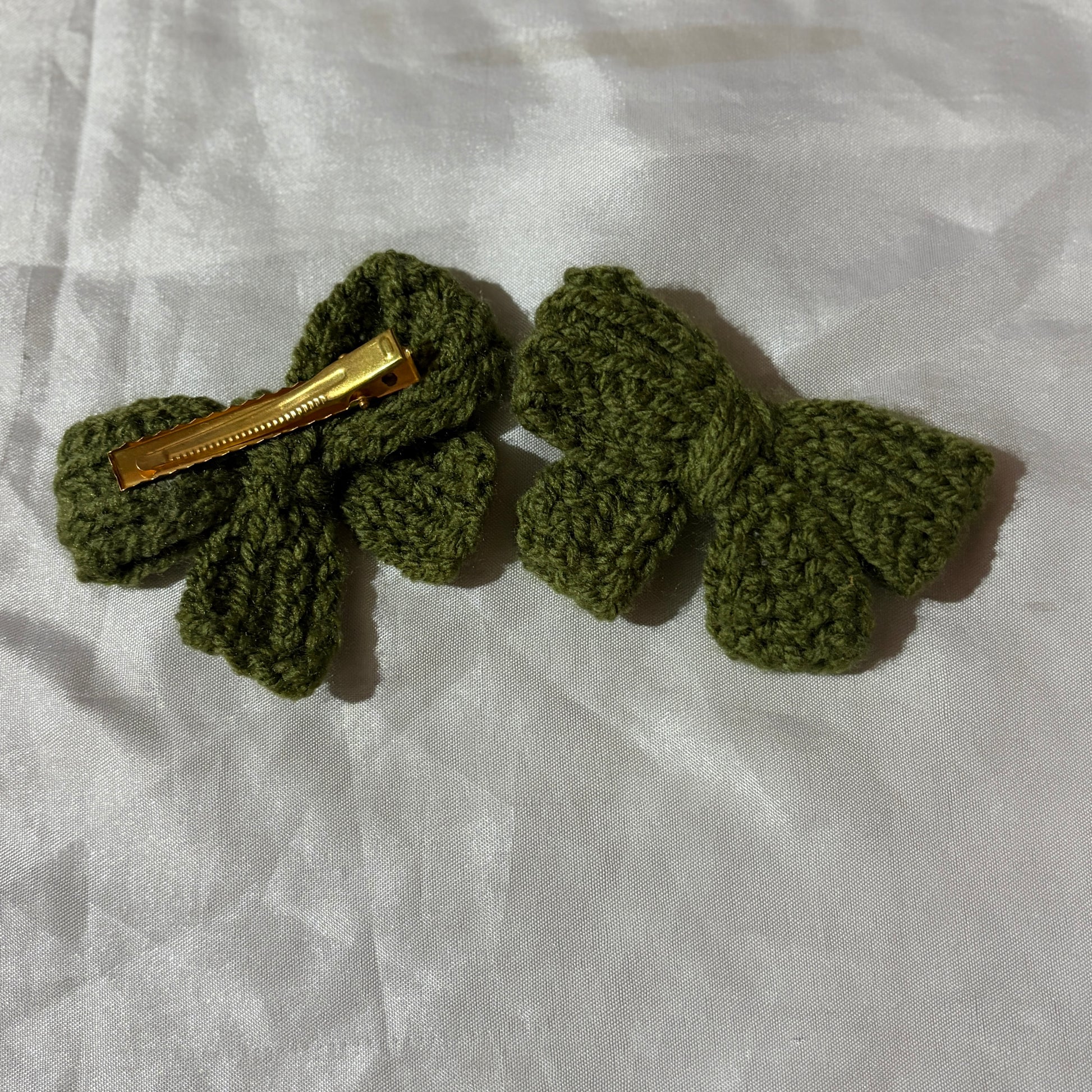 Green crocheted hair clips on a white fabric background