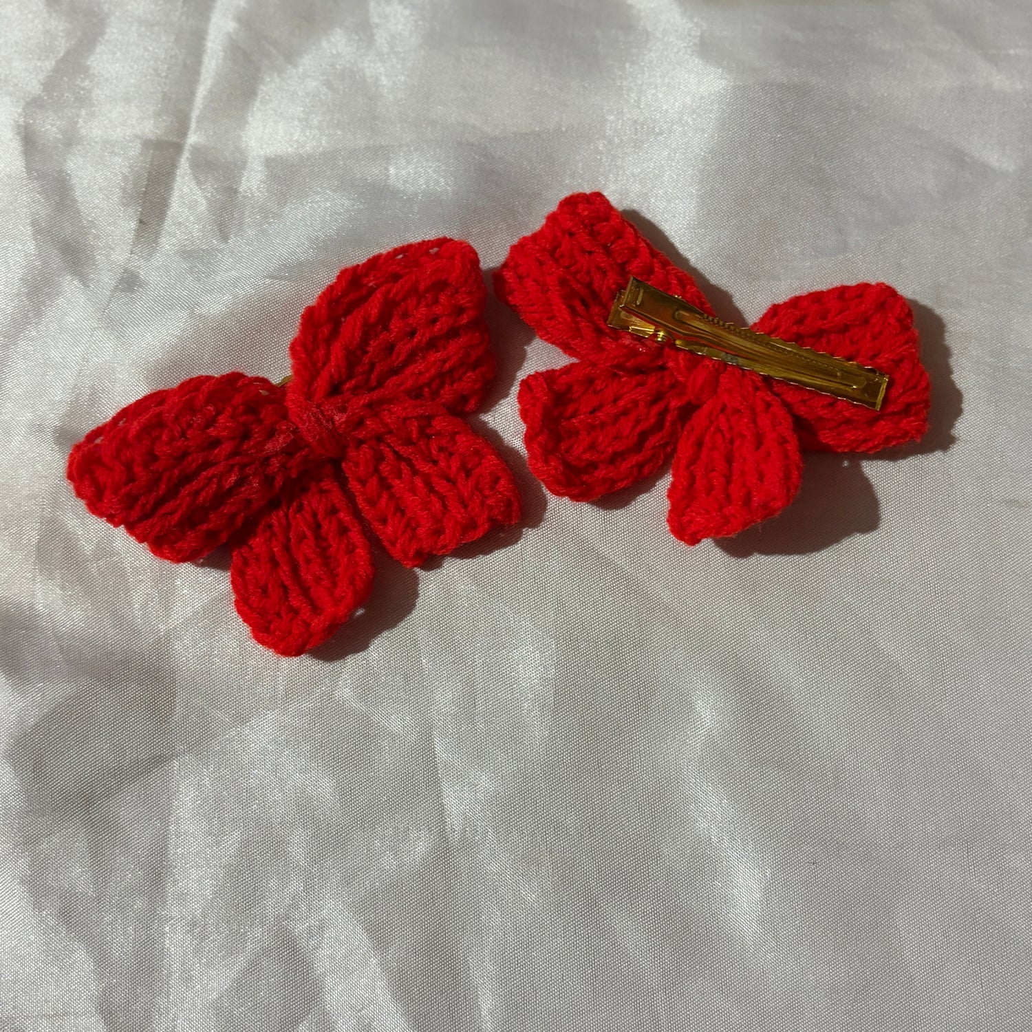 Red crocheted bow hair clip on a white fabric background