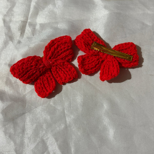 Red crocheted bow hair clip on a white fabric background