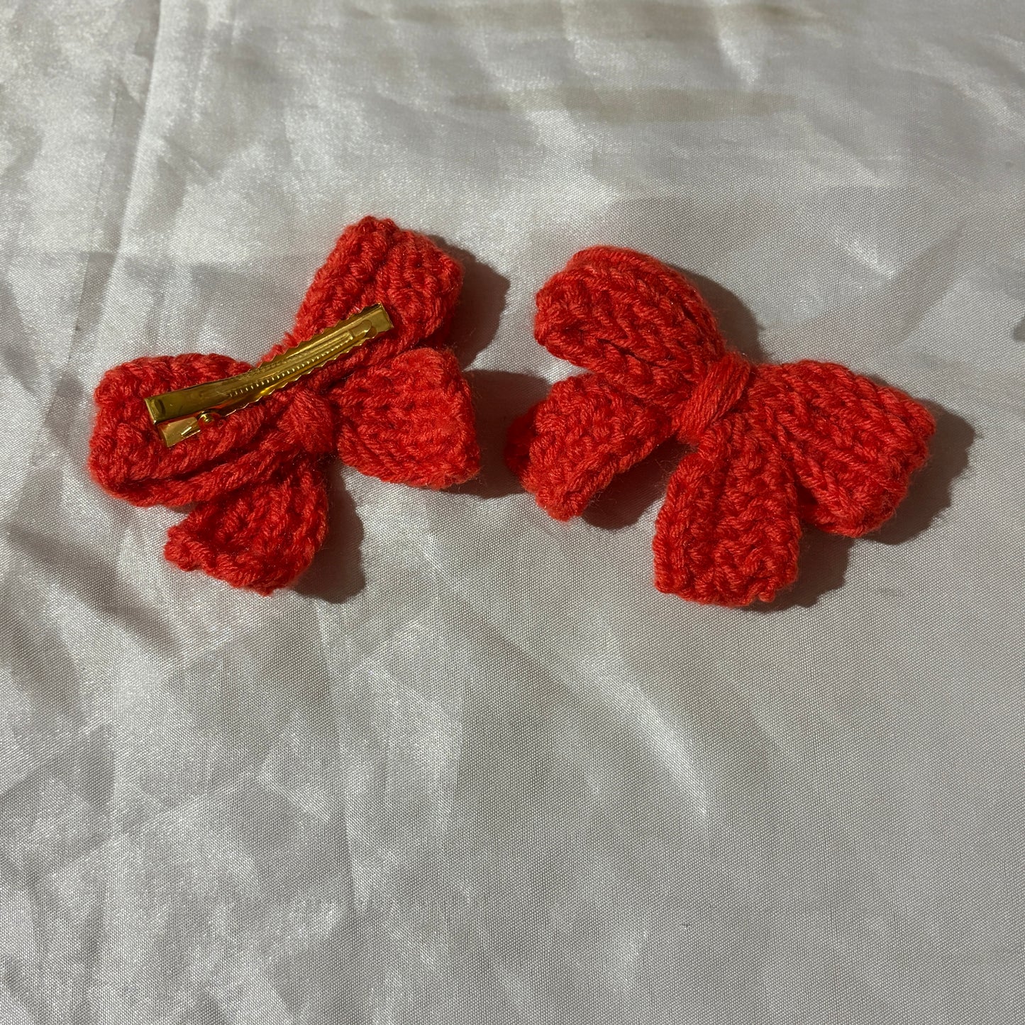 Two red crochet bow hair clips on a light fabric background
