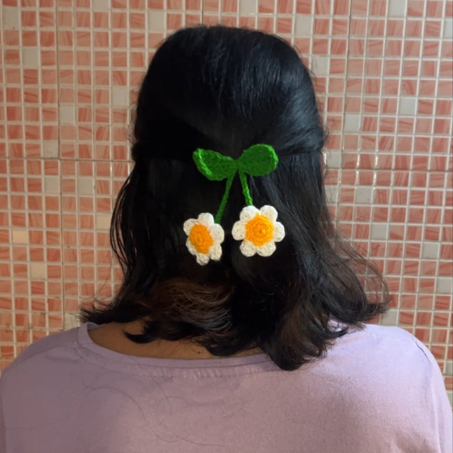 Person with hair accessories including a green bow and yellow flower-shaped clips against a tiled wall background.