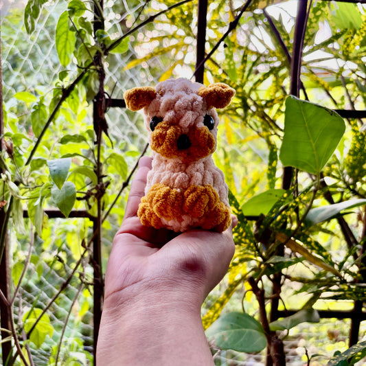 Hand holding a small crocheted puppy dog in front of green foliage