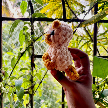 Hand holding a small crocheted puppy dog in front of green foliage