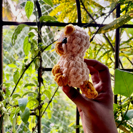 Hand holding a small crocheted puppy dog in front of green foliage