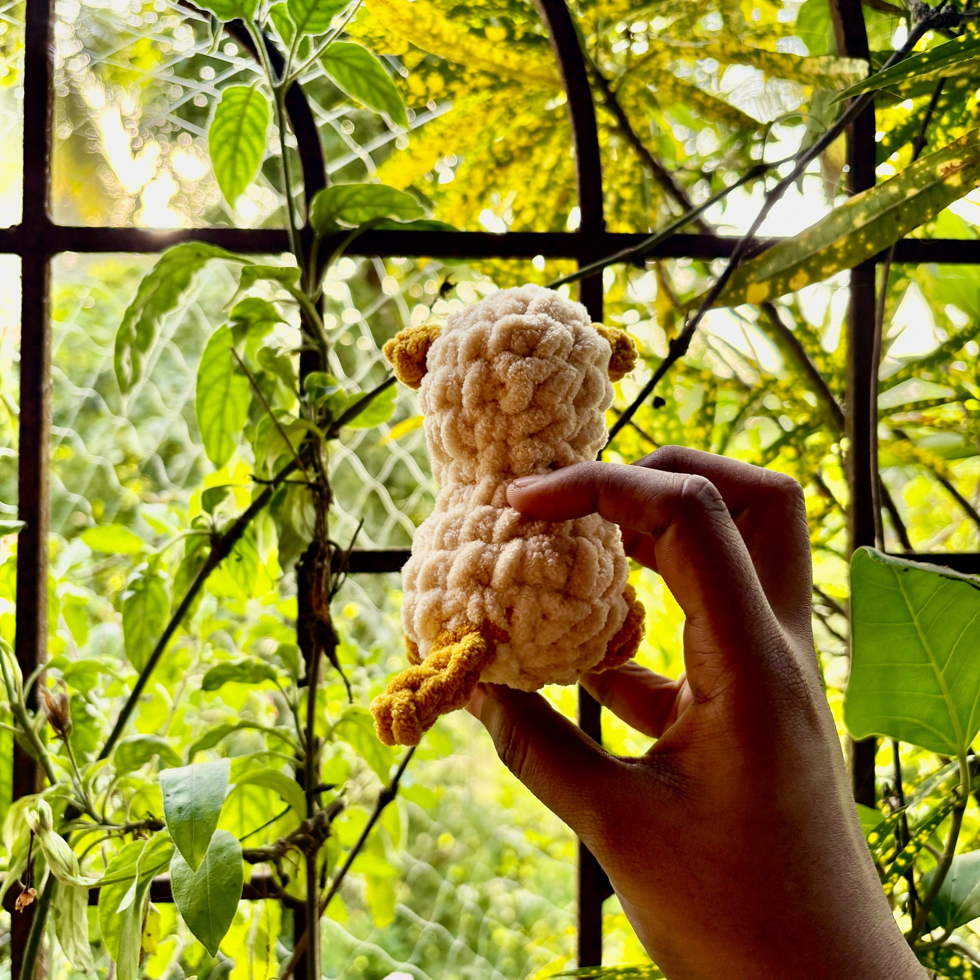 Hand holding a small crocheted puppy dog in front of green foliage
