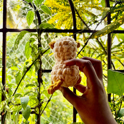 Hand holding a small crocheted puppy dog in front of green foliage