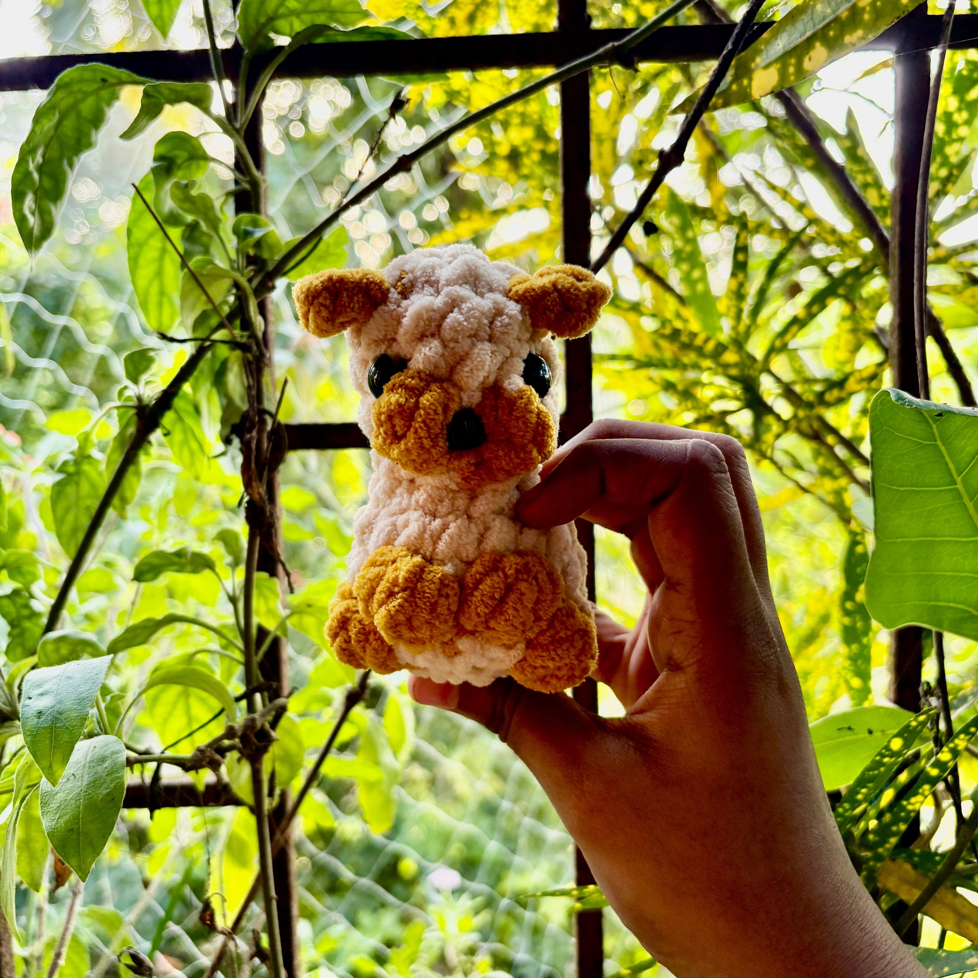 Hand holding a small crocheted puppy dog in front of green foliage
