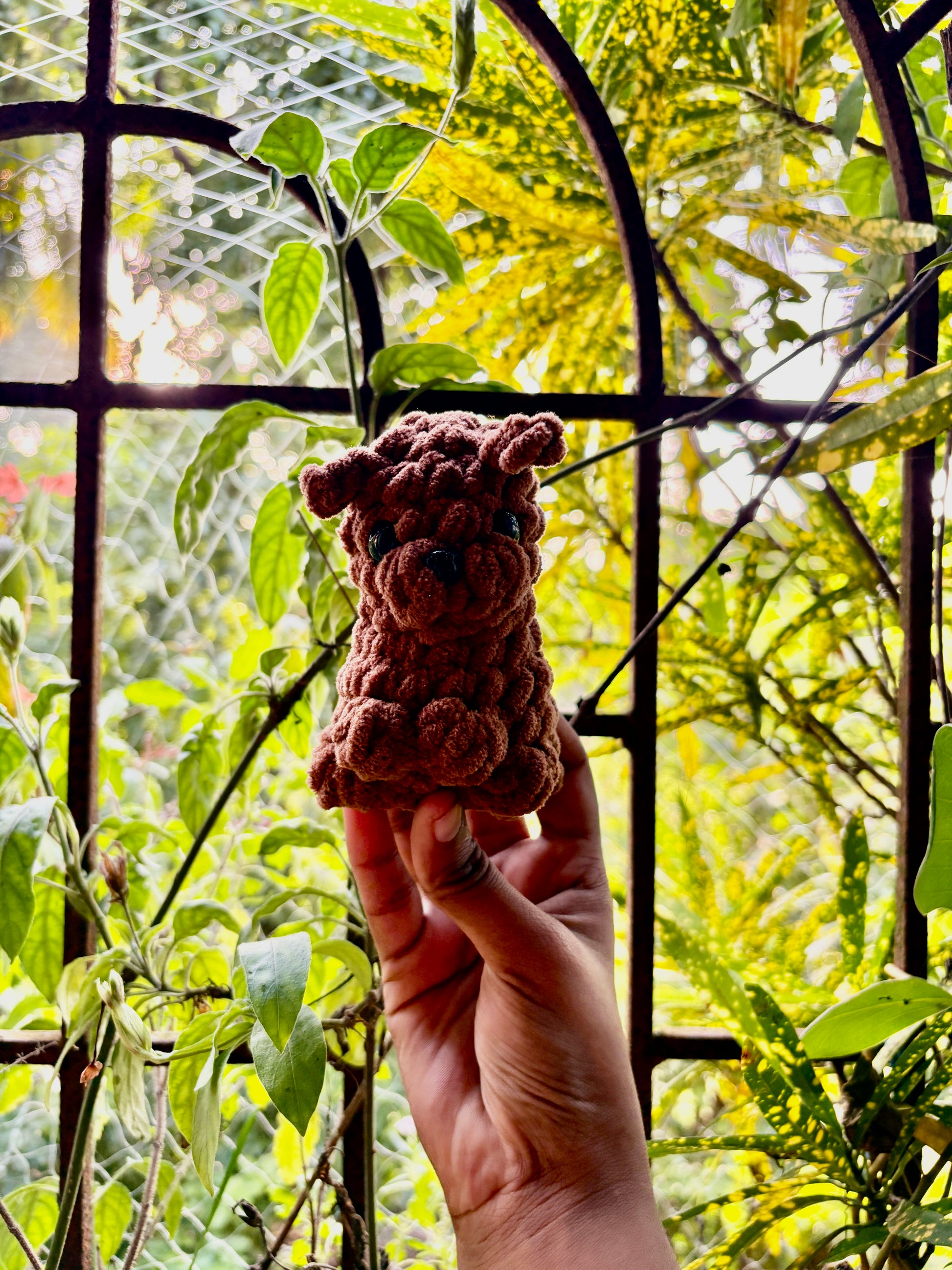 Hand holding a small crocheted puppy dog in front of green foliage