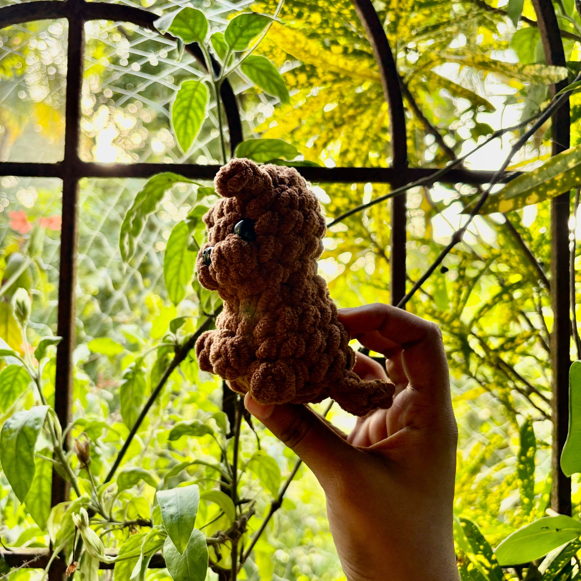 Hand holding a small crocheted puppy dog in front of green foliage