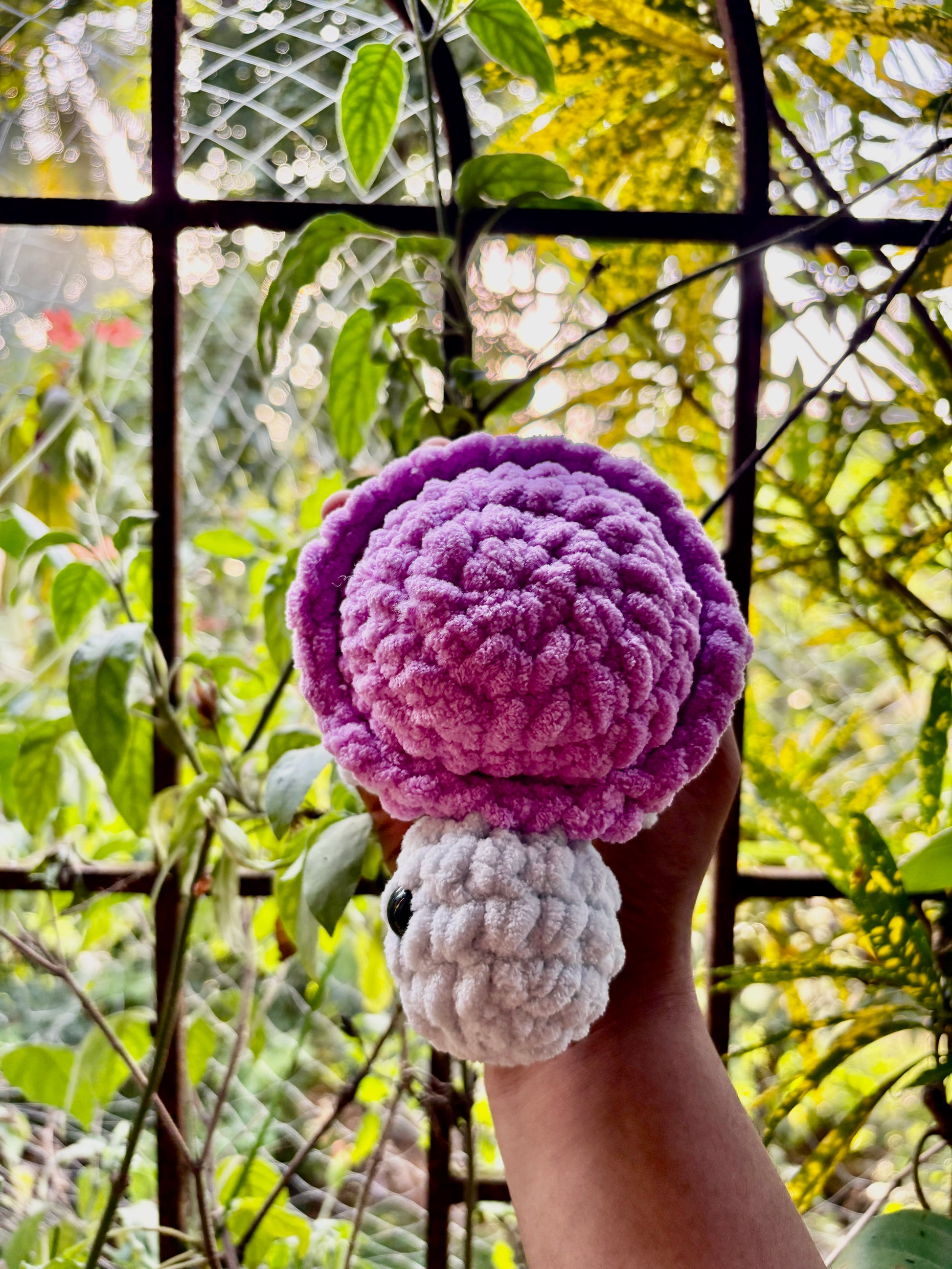 Hand holding a small crocheted turtle with a purple shell against a natural background