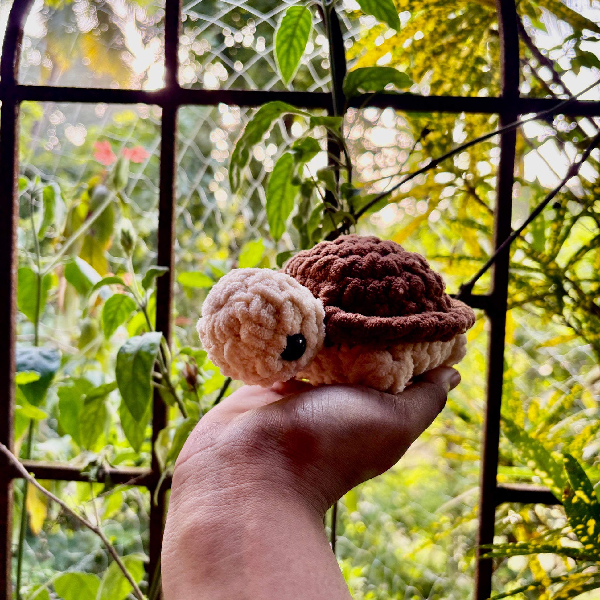 Hand holding a small crocheted turtle with a purple shell against a natural background