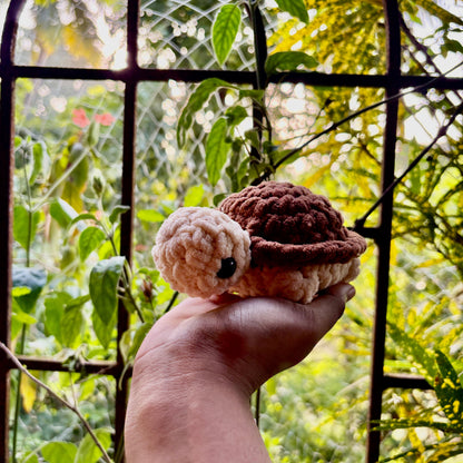 Hand holding a small crocheted turtle with a purple shell against a natural background