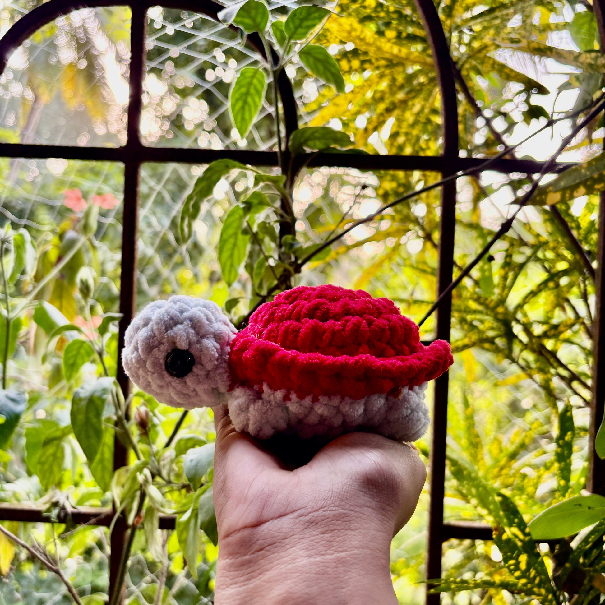 Hand holding a small crocheted turtle with a red shell against a natural background
