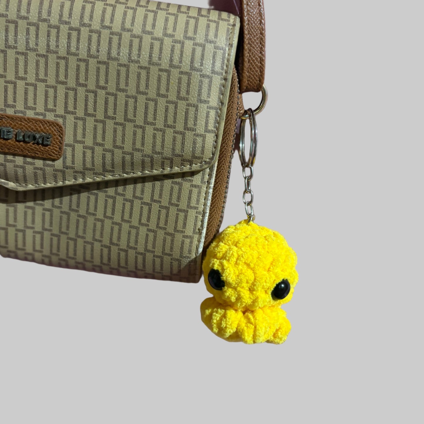 Yellow plush keychain attached to a patterned handbag on a pink surface