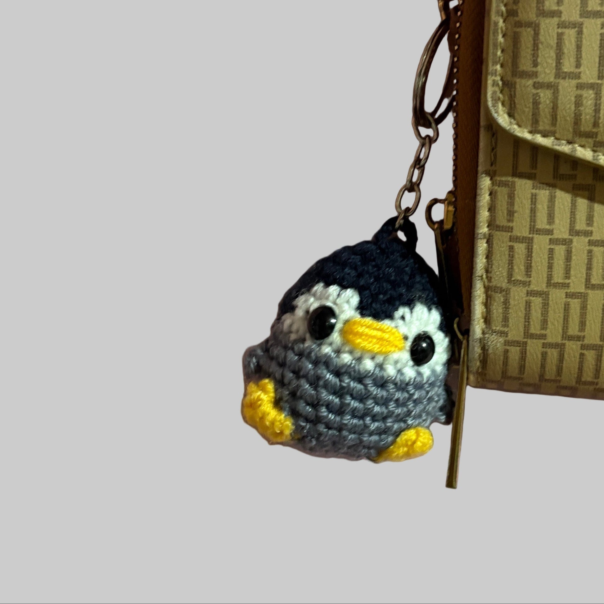 Small crocheted penguin toy next to a Coach wallet on a pink fabric background
