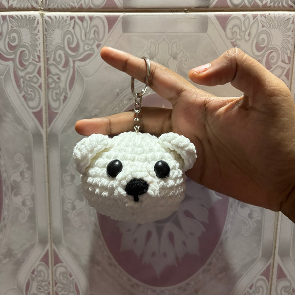 Hand holding a white polar bear-shaped keychain on a patterned tile background