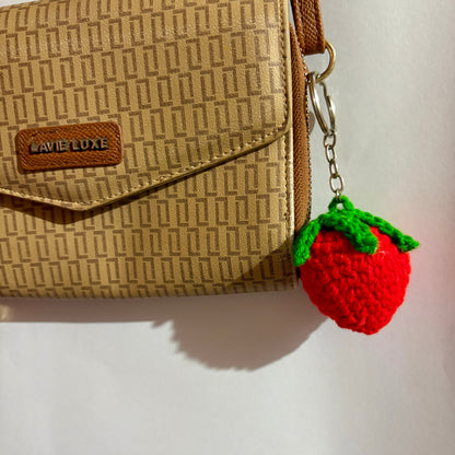 Beige textured handbag with a red strawberry keychain on a light background