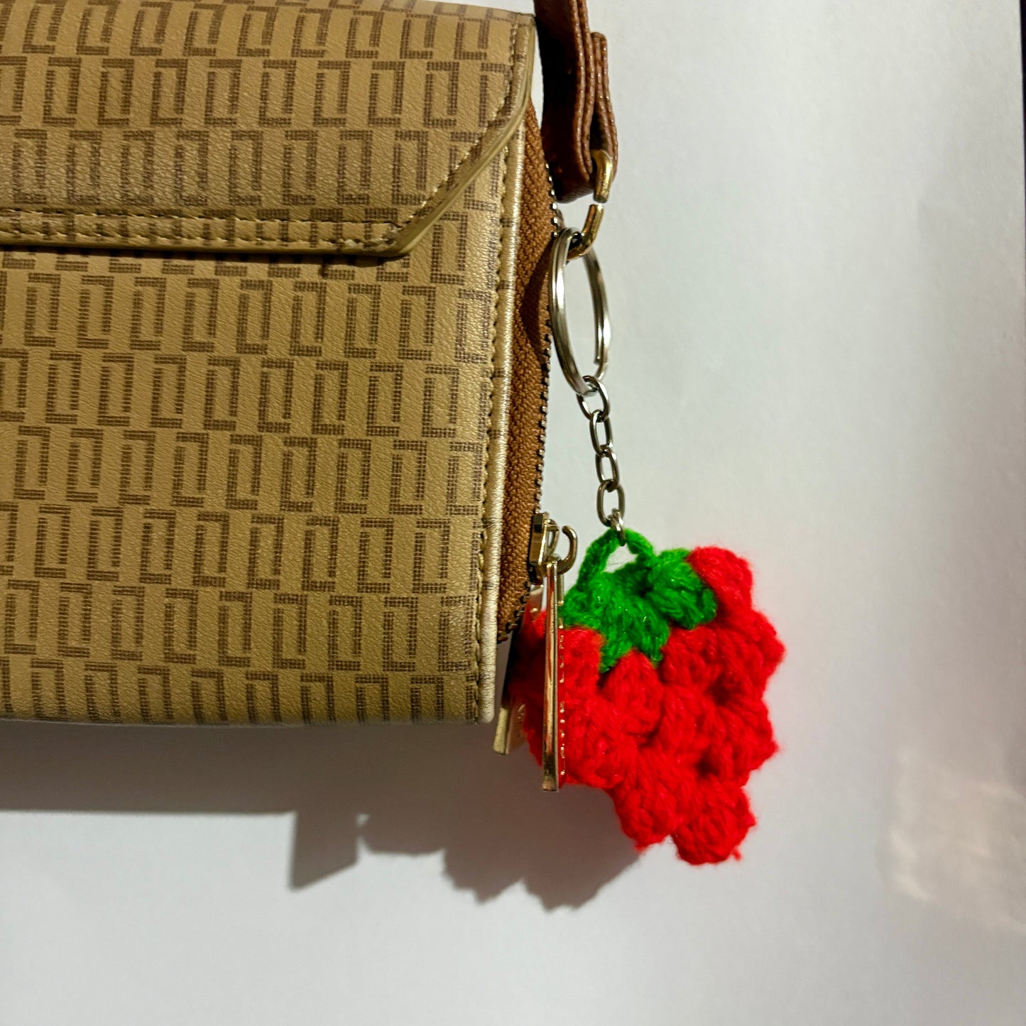 Brown textured handbag with a red and green keychain on a white background